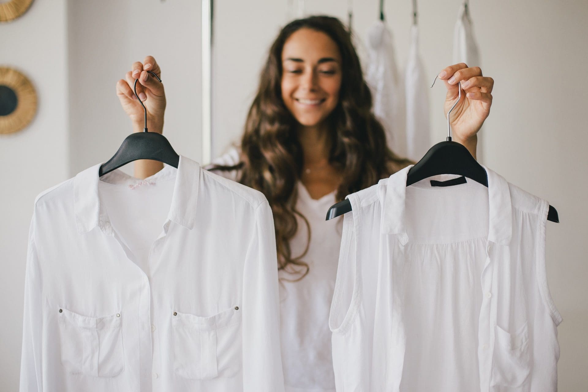 Woman holding two white tops on hangers in front of her.