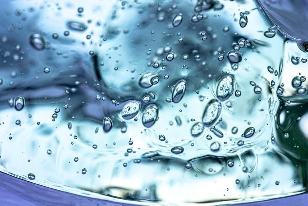 Close-up view of clear blue liquid with suspended air bubbles and light reflections.